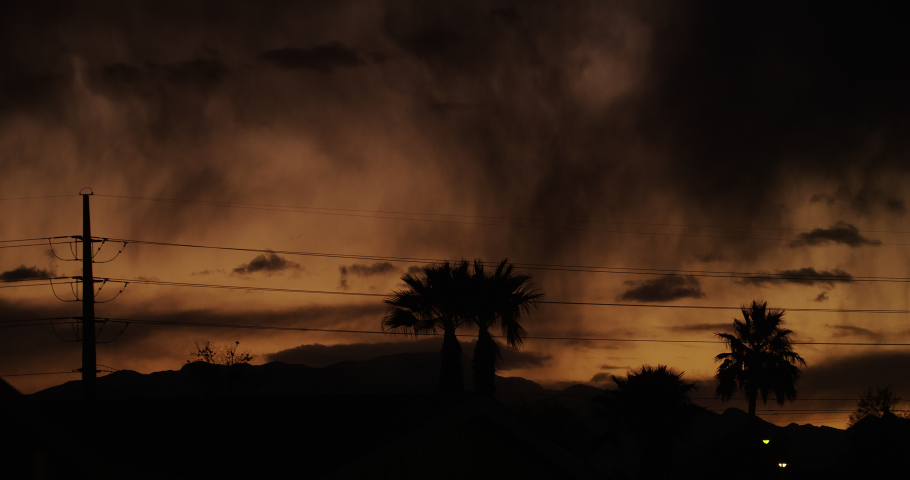Disturbing dream-like vision with shafts of virga, heavy downpour, palm trees and transmission towers in silhouette against the menacing glow of a turbulent sky at dusk.
