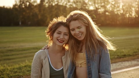 Portrait of young beautiful blonde and adorable asian brunette looking to the camera and smiling. Hipster girls in casual summer clothes posing on background of nature. Positive models having fun