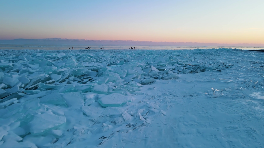 A drone flies over the ice hummocks to tourist group. Hovercrafts in background
