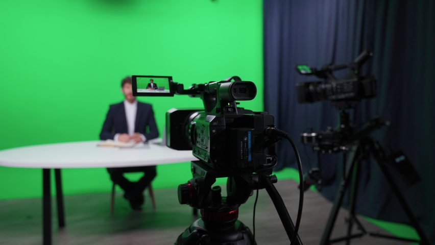 Portrait of an news anchor, man reporter looks into the camera and talks, backstage of studio TV news shooting, chroma key template.