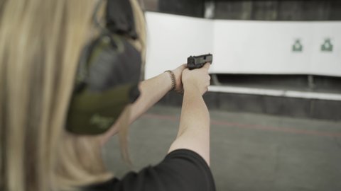 Rear view of a blond woman aiming at a target in a shooting gallery, holding a gun in her hands