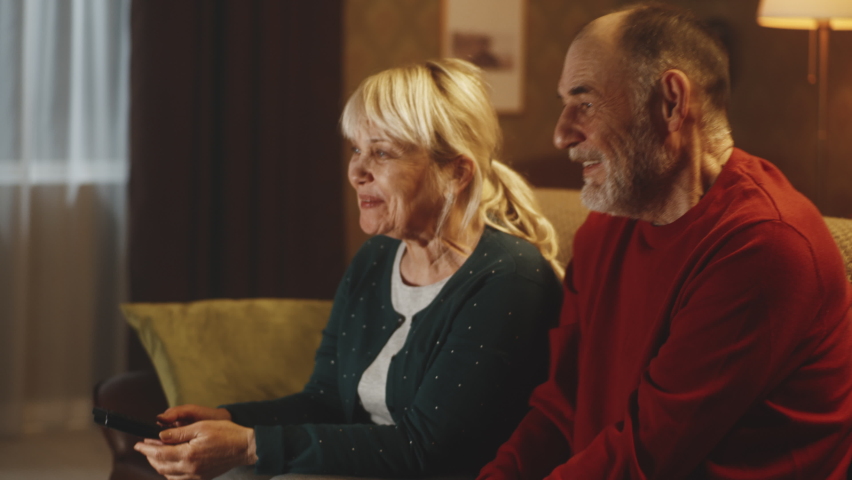 Happy senior husband and wife laughing at funny joke while sitting on couch and watching comedy on TV at night at home Royalty-Free Stock Footage #1088456265