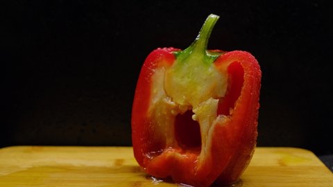 Moving camera video on slider forward on cut bell pepper on with dripping olive oil on black background