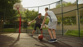 People playing street basketball during a warm summer day. Two teens playing a basketball match on an outdoors court during a sunny summer day. Attack and defence, missed shot.
