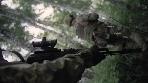 Close-up action shot, armed special forces soldiers with Kalashnikov assault rifles on a special operation in a dense deciduous forest protect the front line