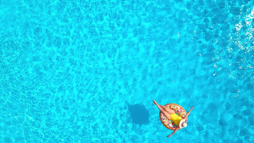 Aerial view of man dives into the the pool while girl is lying on a donut pool float