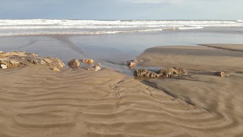 Deserted sandy beach with destroyed stone breakwater after storm