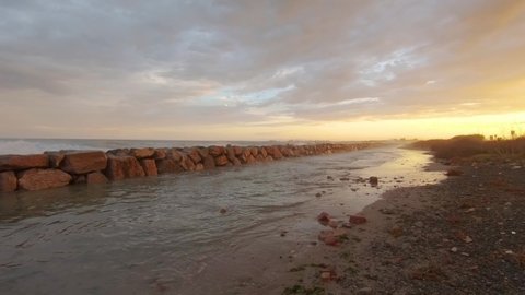 Stone breakwater on sandy seashore in autumn evening on sunset