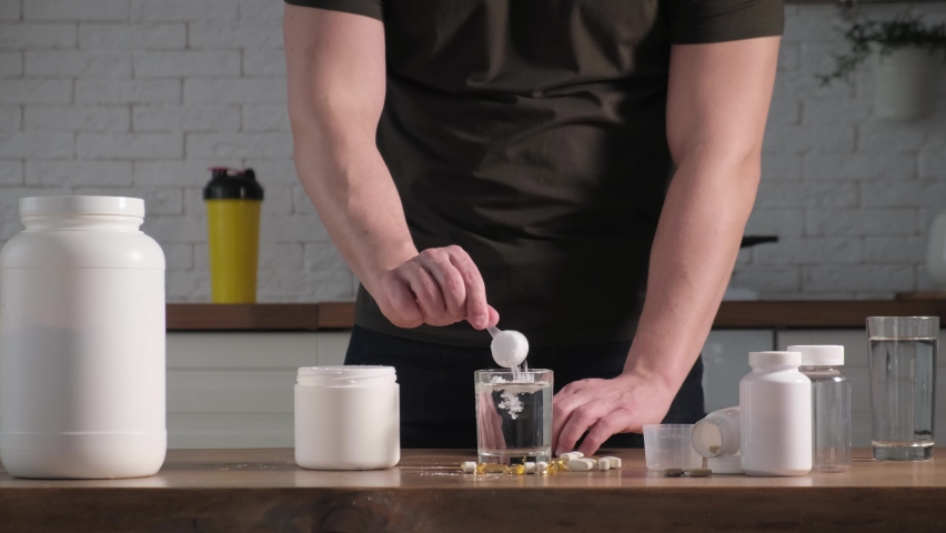 A man adds a serving of creatine or aminocysts to a glass of water. Concept: sports supplements, nutrition, bodybuilding, fitness Royalty-Free Stock Footage #1088461711