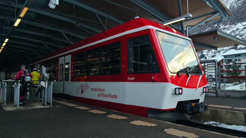 Zermatt, Switzerland - February 24, 2022: Matterhorn Gotthard Bahn Red Train with passengers departing from Täsch Station. Beautiful Train in Jungfrau Region Switzerland with people with ski in winter