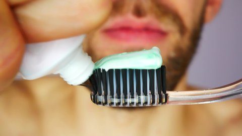 Close-up of a black toothbrush and a young man squeezes toothpaste onto it
