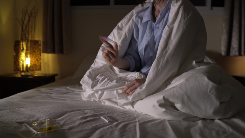 Closeup view of female hands making express covid19 antigen test sitting on a bed at home. A young caucasian woman is shaking a tube and dripping reagents to detect coronavirus. Diagnosis and medecine