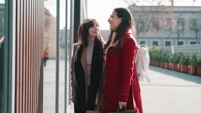 Video of two beautiful friends talking and having fun while walking on the city street with shopping bag.