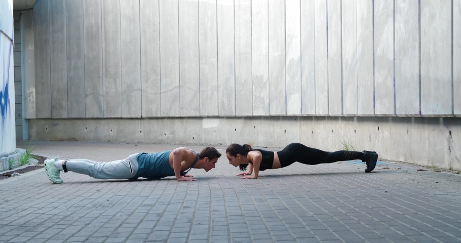 Sporty couple, man and woman are doing push ups together and touching their hands, outdoors. Group training and healthy lifestyle concept Royalty-Free Stock Footage #1088466627