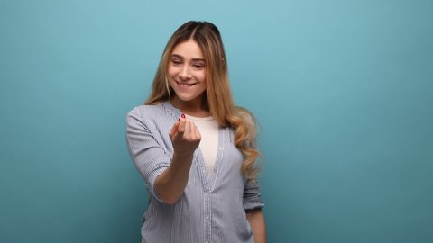 Come here. Portrait of attractive woman making beckoning gesture, inviting to come, flirting and looking playful, wearing striped shirt. Indoor studio shot isolated on blue background.