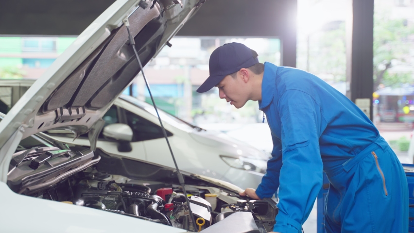 Asian automotive mechanic man open a car hood and check up the engine. Attractive vehicle service manager worker work in mechanics garage, check and maintenance to repair the motorcar car in workshop. Royalty-Free Stock Footage #1088471819