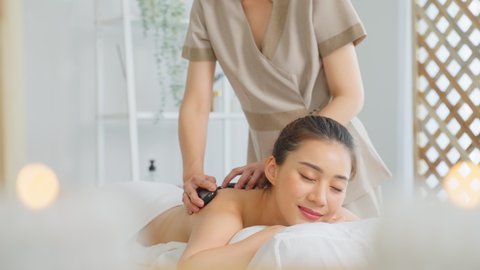 Asian young relaxing woman getting back massage therapy with hot stone. Attractive beautiful girl lying on massage table, getting physiotherapy from masseuse for skin and body care in spa beauty salon