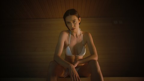 Beautiful Caucasian Female Model Sitting in the Sauna and Posing in a Slow Motion Frame. Gorgeous Brunette Looking Directly at the Camera in a Hot Sauna.