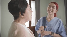 Asian woman nurse wearing scrubs talking with Senior Asian woman in the bedroom. Caregiver visit at home. Home health care and nursing home concept. Slow-motion 4k video.