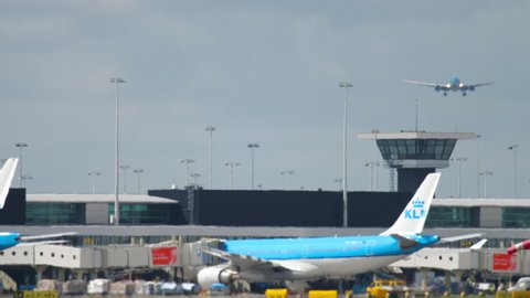 AMSTERDAM, THE NETHERLANDS - JULY 25, 2017: Long shot, Boeing 777 KLM approaching to land at Schiphol Airport. Airport terminal, boarding passengers on board and loading and unloading luggage