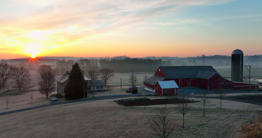 Rural family farm and red barn scene in winter sunrise. Rising aerial establishing shot for agriculture in Pennsylvania USA. Lancaster County.