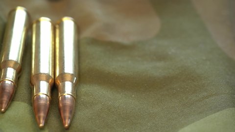Large caliber 3006 cartridges laying on camouflage military jacket - Slider from right to left