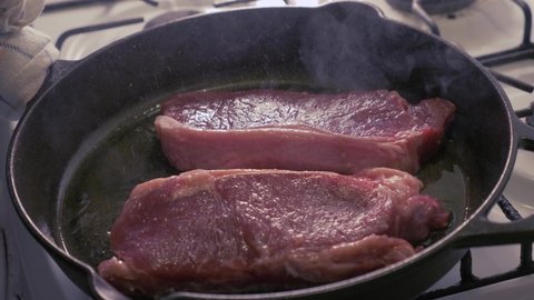 Steaks being cooked in a cast iron skillet with oil - slow motion