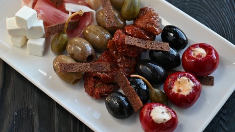 Plate of snacks on black wooden background. Olives croutons sun-dried tomatoes capers, bacon cheese and stuffed peppers with cheese on a plate