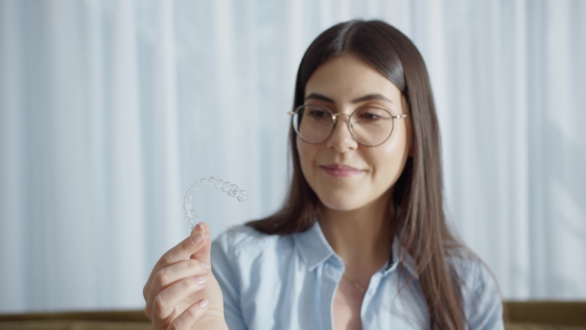 Happy Attractive Woman Smiles And Sitting In Cozy House And Holding Invisalign Braces. Putting On Transparent Plastic Retainers Or Tooth Whitening System. Concept Of Dental Healthcare And Orthodontic Royalty-Free Stock Footage #1088478437