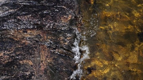 Slow motion shot of clear lake water lapping against granite rock. Muskoka, Ontario, Canada.