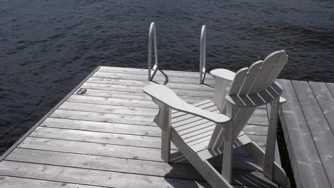 Slow motion vacation dock. Muskoka or Adirondack chair on wooden dock with slow motion water.