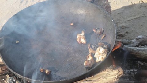 A close up shot of abalone shellfish frying on a pan on a beach campfire.