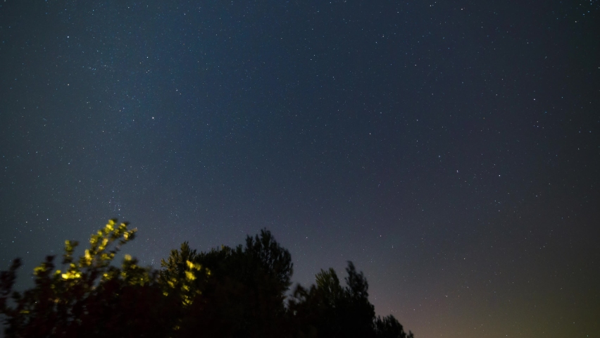 The stars move around the North Star. The treetops in the foreground. Time lapse of star trails in the night sky in Italy. 4K