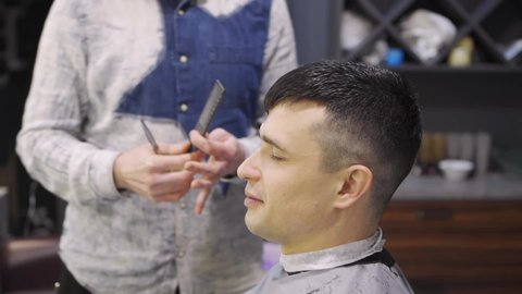 the hairdresser makes a haircut for a brunette man with a scissors in a barbershop. professional services. beauty salon for men. cosmetics and products for scalp and hair care.