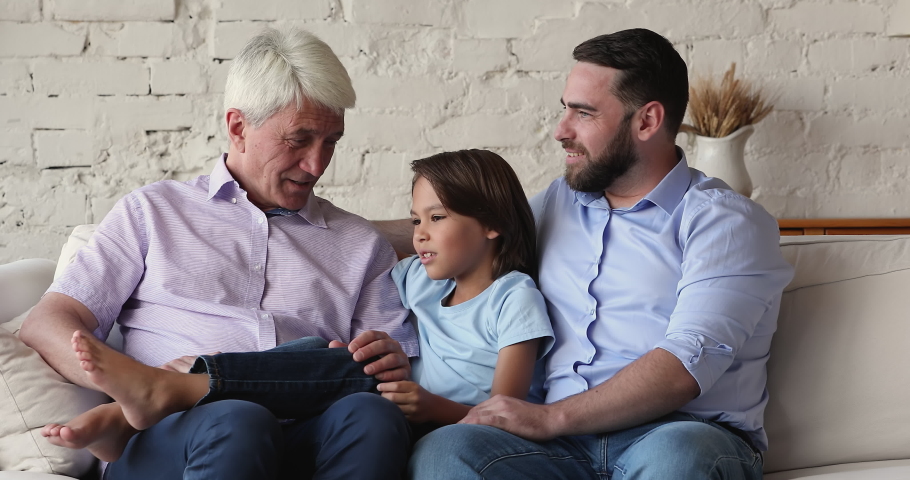 Little cute boy his grandfather and dad spend time, talking sit on cozy sofa, having good relation, enjoy warm conversation relaxing together at home. Multi generational family ties, offspring concept Royalty-Free Stock Footage #1088486871