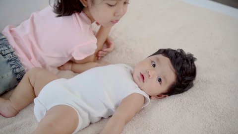 Slow motion of Elder sister kissing newborn baby while lying on bed, adorable girl kiss cheeks toddler with love and care. cute little girl play with brother after him wake up. Family and Healthy.