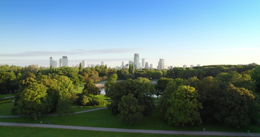 City park with the city center in the background. Lake in the city park with green nature trees during summer morning. Aerial view of offices in skyscrapers over the panorama of Warsaw in a urban park Royalty-Free Stock Footage #1088489111