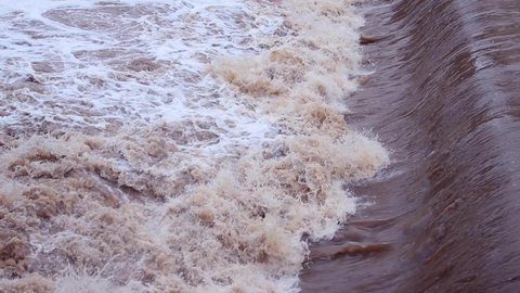 Slow motion side view of splashing dirty brown water under a weir