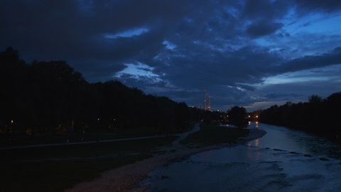 Munich nature at dramatic dusk: autumn in park of tourist Bavarian city. View of Isar river, trees and St Maximilian church from Reichenbach Bridge. Munchen, Bavaria, Germany. Camera horizontal pan