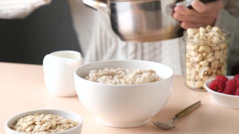 Healthy breakfast, woman serving cooked oatmeal porridge in bowl. Vegan diet, clean eating concept