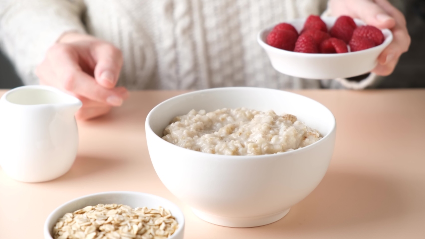 Oatmeal porridge with raspberries for breakfast. Woman adding fresh raspberries into cooked oatmeal bowl Royalty-Free Stock Footage #1088492831