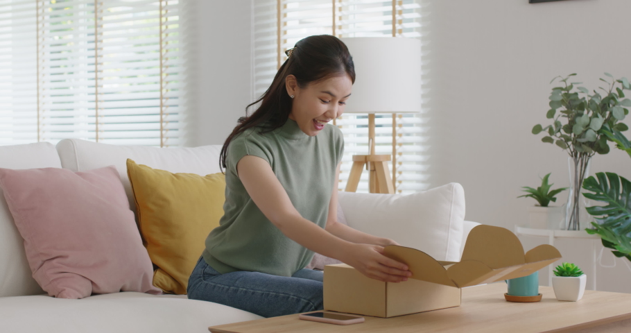 Young happy asia people teen girl smile enjoy unbox post mail sit relax at home comfort sofa couch feel joy amazed awe wow in omni channel fast send parcel via online sale shop store e-commerce order. | Shutterstock HD Video #1088493155