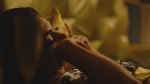 Side view of beautiful sexy woman laying on luxury bed with golden color satin linens . Caressing , touching her body . Portrait of girl lies and looking at camera . Hotel room . Slow motion close up 