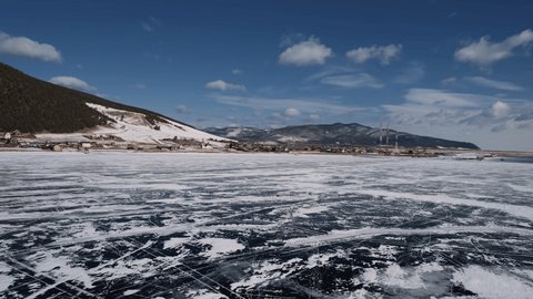 Ice, frozen Lake Baikal in winter. Pieces of ice and snow, mountains on the background. Clear sunny day, blue sky. A trip to Lake Baikal. Top view, shooting from a drone. village on the lake shore