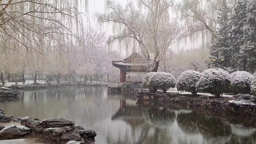 Chinese pavilion surrounded by pond and trees on snowy day, Beijing China.