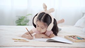 Cute primary school age girls drawing coloring picture with pencils on bed in holiday. Adorable child enjoying creative art hobby activity at home, children development at home concept. 
