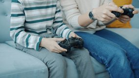 Tilt-up slow motion of mother and son playing video game with joysticks laughing doing high-five indoors at home. Family and entertainment concept.