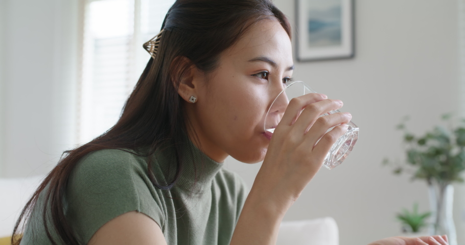Asia people young woman happy relax smile sit at home sofa drink water take birth control pill pouring folic preconception drug bottle or weight loss diet capsule. Body skin health care sick relief.