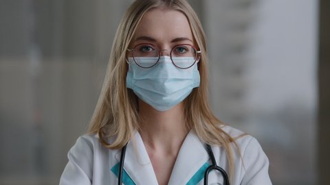 Caucasian doctor specialist nurse woman practitioner therapist in glasses sits in clinic hospital at table take off facial protective medical mask end of working day recovery finish covid pandemic