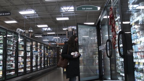 BATTLE GROUND, WASHINGTON  USA - MARCH 2022: Moving shopping cart finds woman in frozen food aisle in grocery store who buys ice cream.